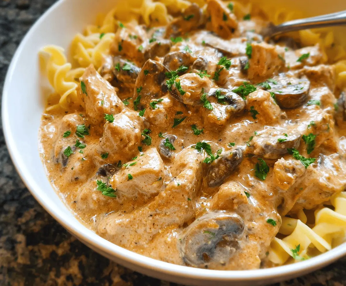Creamy chicken stroganoff served over noodles with mushrooms and herbs on a white plate, ready to enjoy