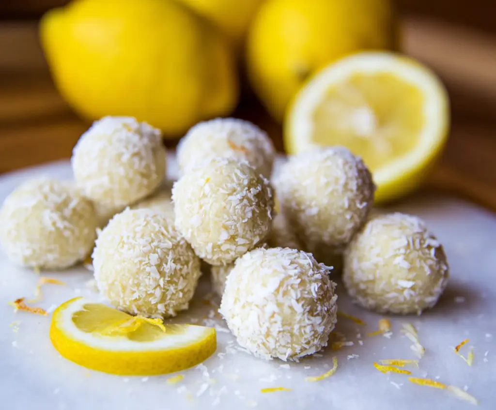 Healthy lemon coconut protein balls on a white plate with fresh lemon slices and shredded coconut for a nutritious snack.