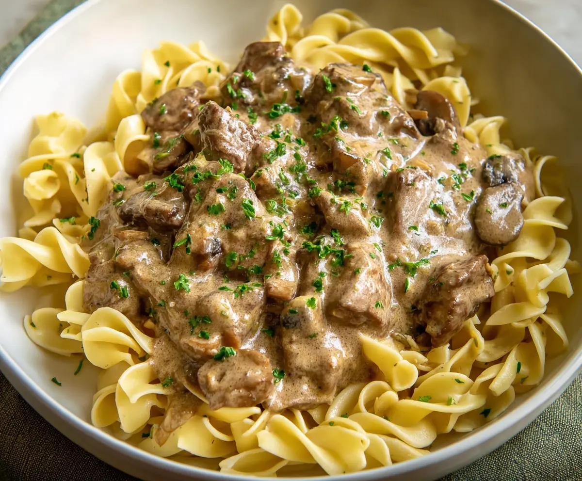 Creamy Beef Stroganoff served over tender egg noodles, garnished with fresh herbs.