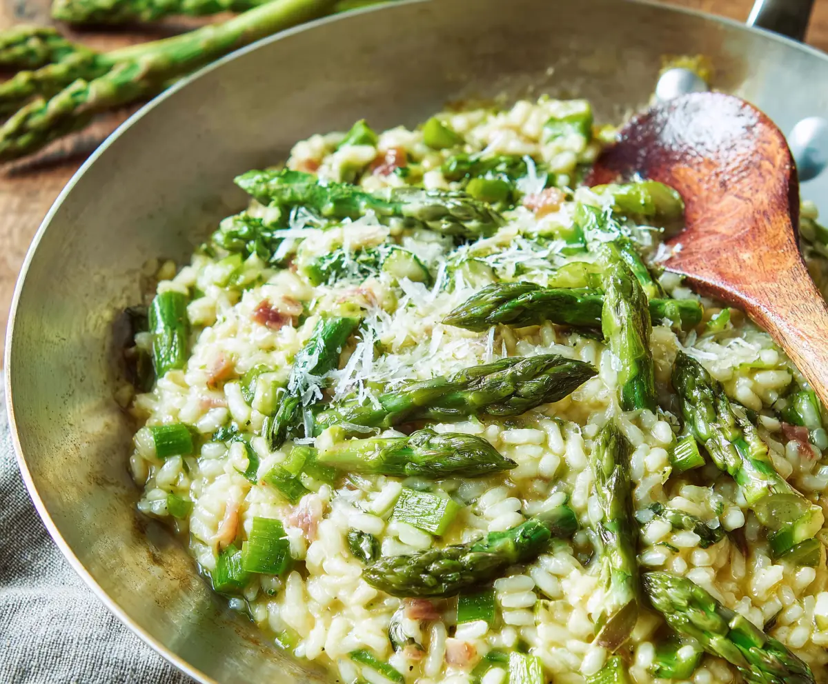 Creamy asparagus risotto garnished with fresh herbs on a white plate.