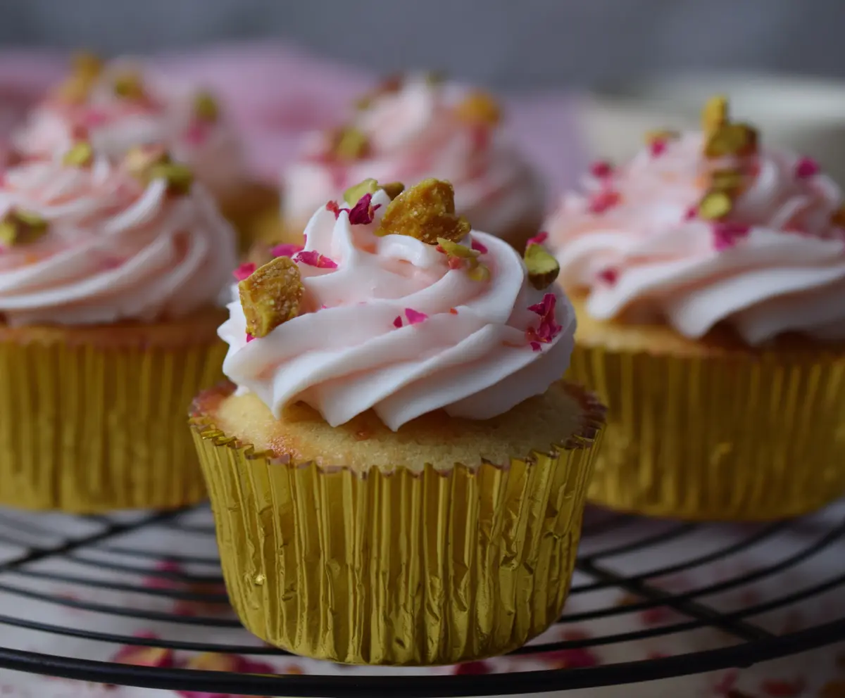 Delicious honey pistachio rosewater cupcakes decorated with pink rose petals, perfect for special occasions.